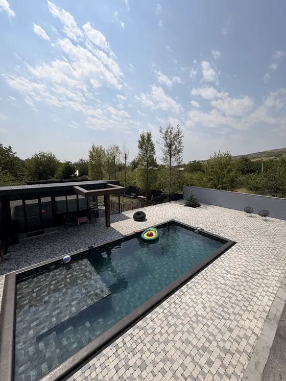 Black Inn Ashtarak-ի ընդհանուր տեսքը՝ կանաչ ծառերով, լողավազանով և մուգ շենքով